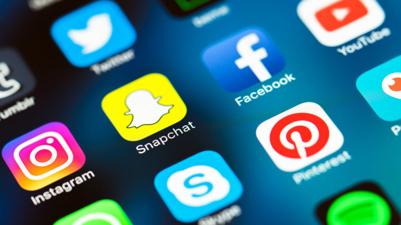 Close-up of social media app icons on a phone screen, including Instagram, Facebook, Snapchat, Twitter, YouTube and Pinterest.
