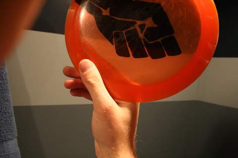 A one-finger grip on an orange disc, a single finger hooked under the rim.