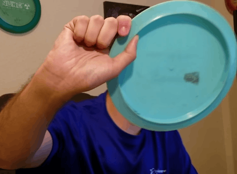 A tomahawk grip on a teal disc held vertically, the thumb inside the rim.
