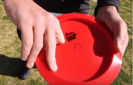 A power grip on a red disc, the thumb flat on top and the fingers gripping underneath.