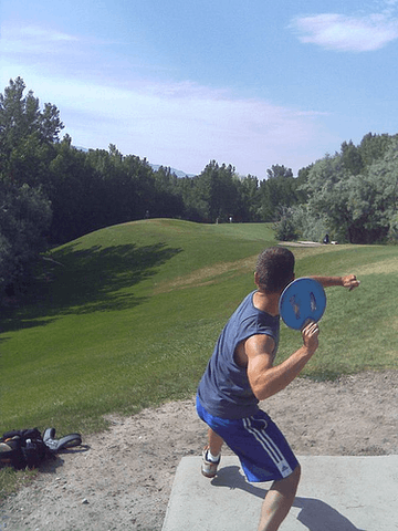 A player winding up to throw a blue disc from a tee pad on a grassy fairway.