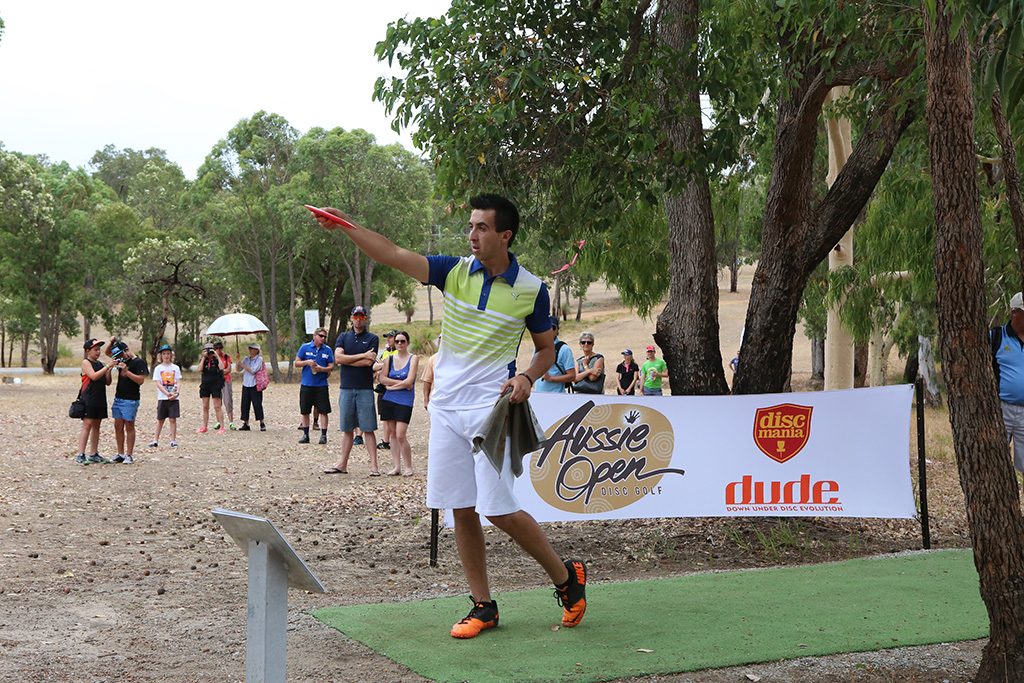 A player throwing from a tee pad at the Aussie Open, with spectators and event banners lining the fairway.