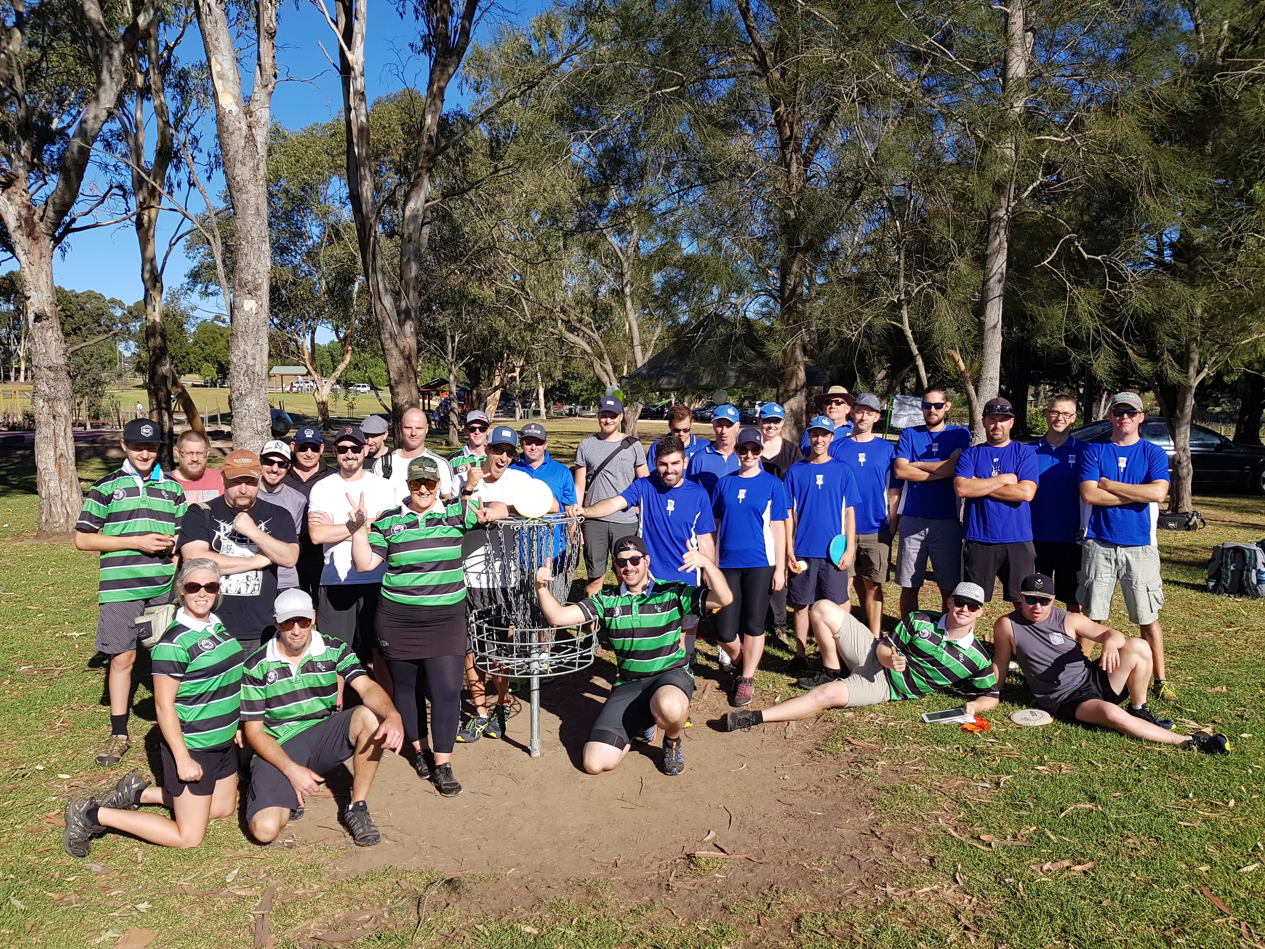 A large group of players in club shirts posing together around a basket after a round.