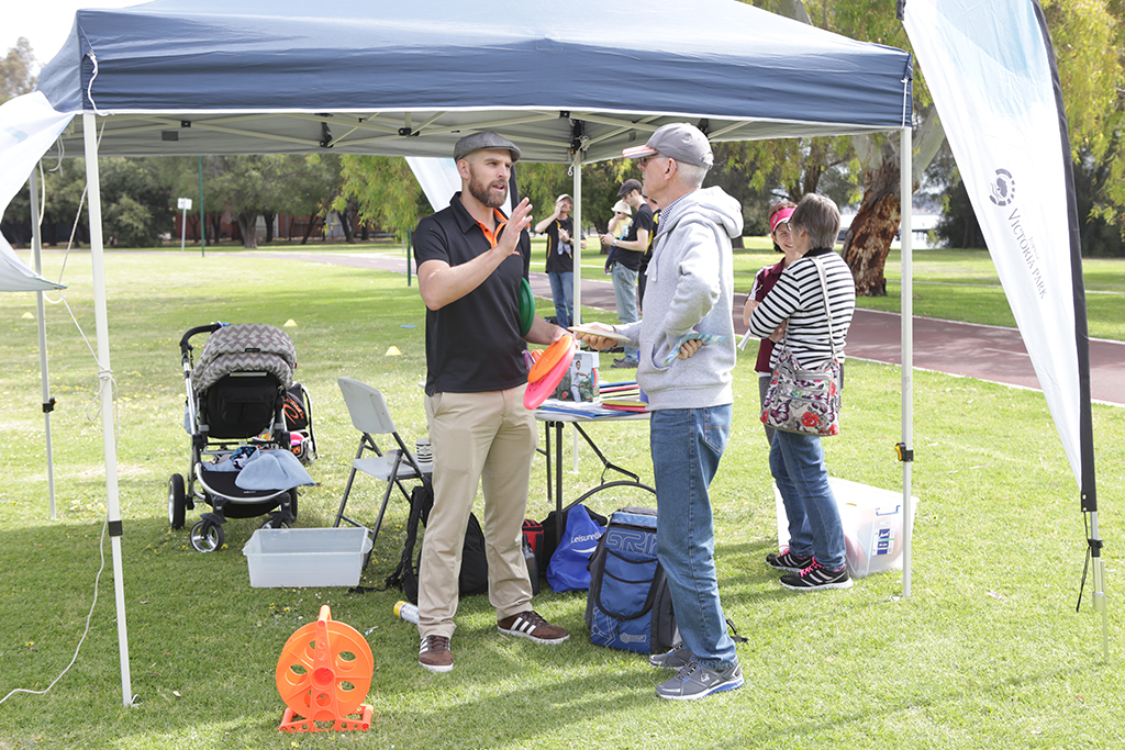A come-and-try setup on grass: a marquee, equipment table and people chatting beside a portable basket.