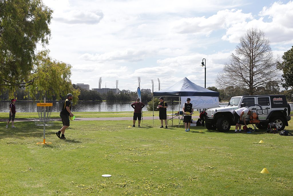 A riverside park set up for a come-and-try day, with a marquee, vehicle and players on the grass.