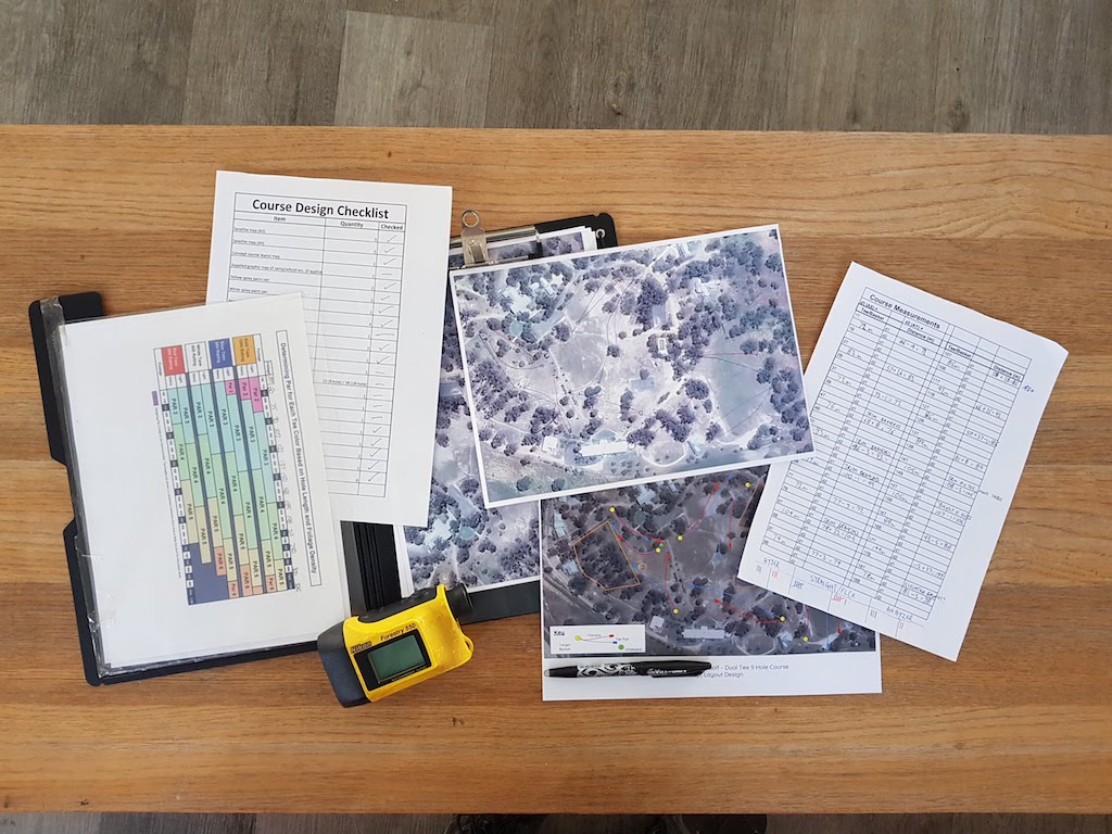 A course design checklist, aerial site photographs, a laser rangefinder and a pen laid out on a desk.