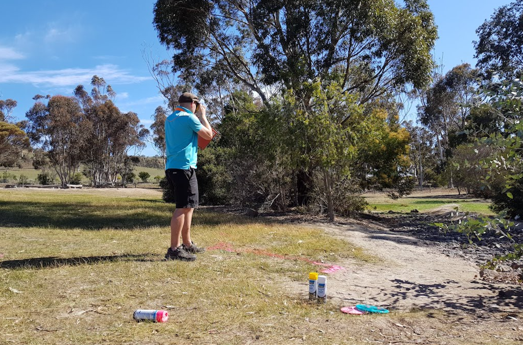 A course designer standing on an open bushland site, sighting a line where a hole will run.