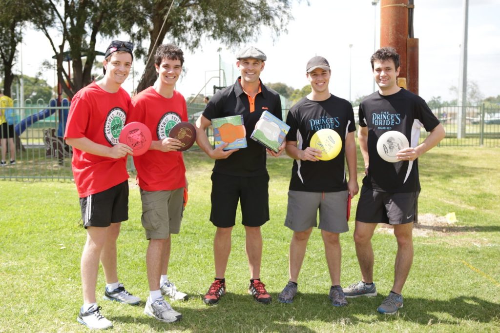 Five young players in team shirts holding discs and posing together on a sports field.