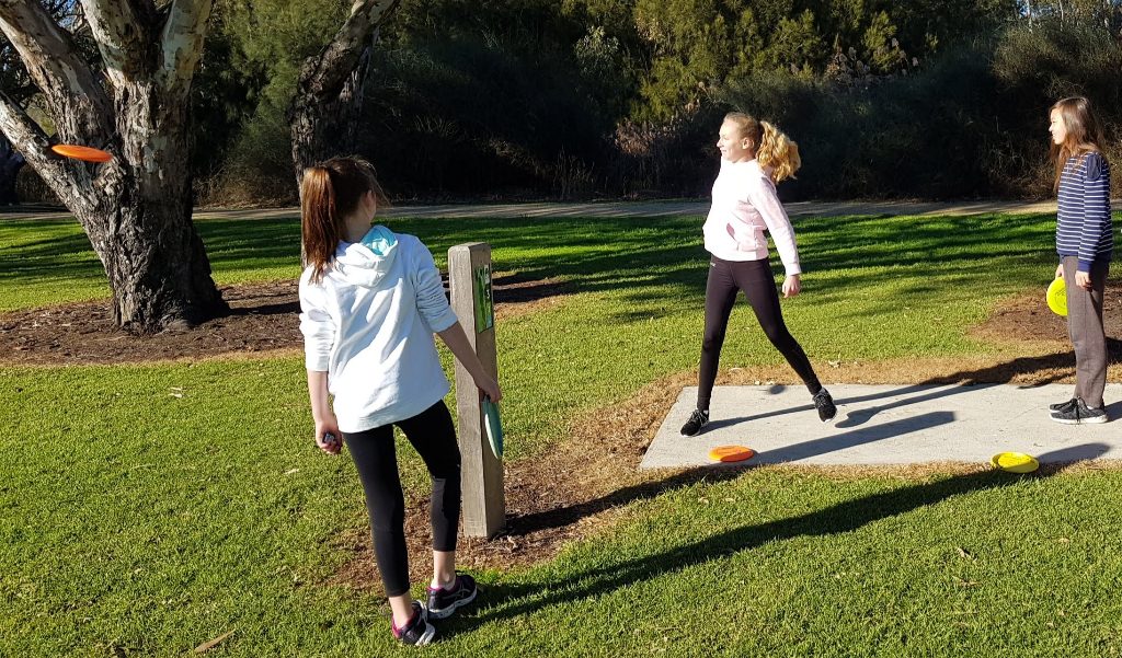 Two girls standing beside a concrete tee pad on a grassy course.