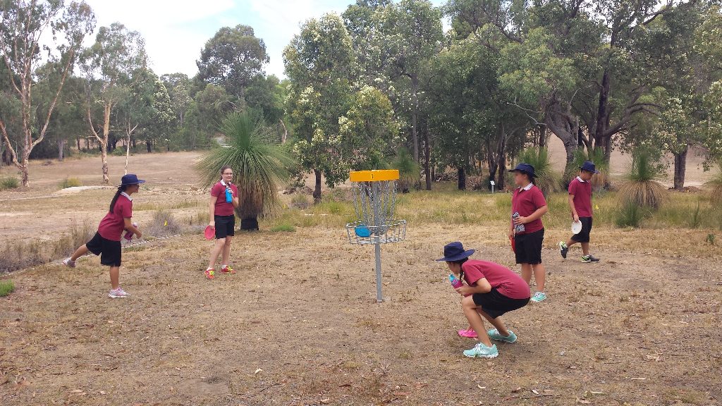 School children in maroon sports uniforms playing around a basket on a dry course.