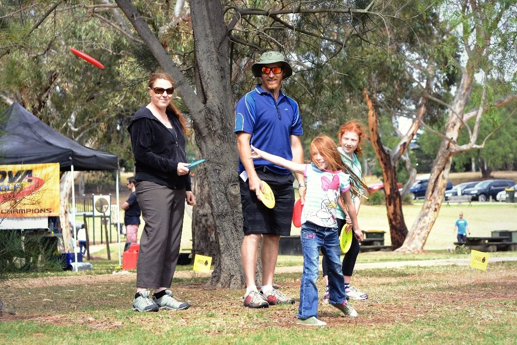 A family collecting discs at a come-and-try stand set up under a tree.