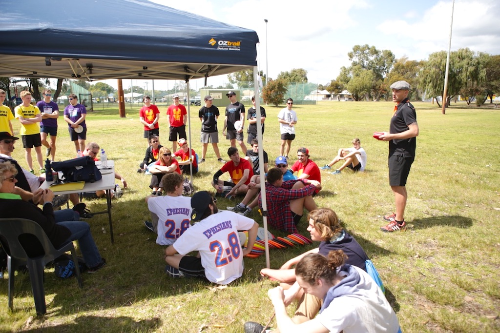 Players resting under a marquee between rounds at a tournament, scorecards and bags on the grass.