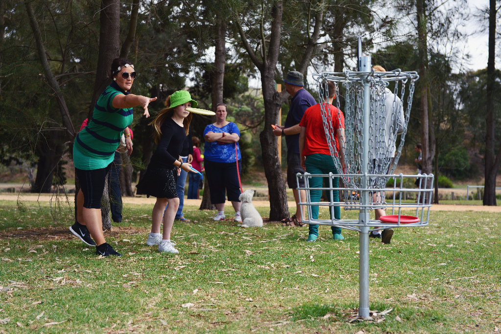 Players gathered around a basket in bushland, one throwing towards it.
