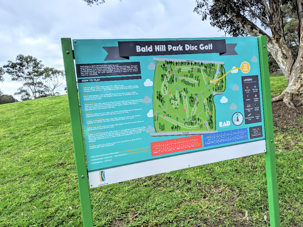 Information board for Bald Hill Park Disc Golf mounted on green posts, showing the course map and how to play.