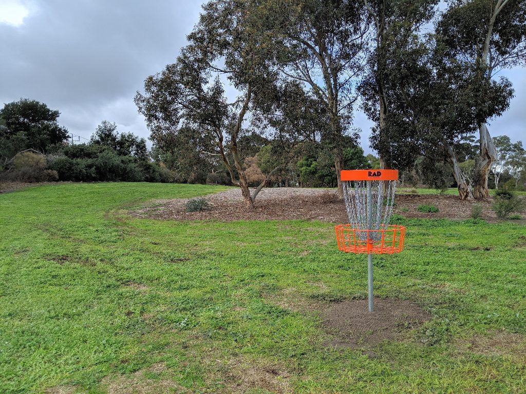 An orange-topped disc golf basket standing on mown grass among gum trees.