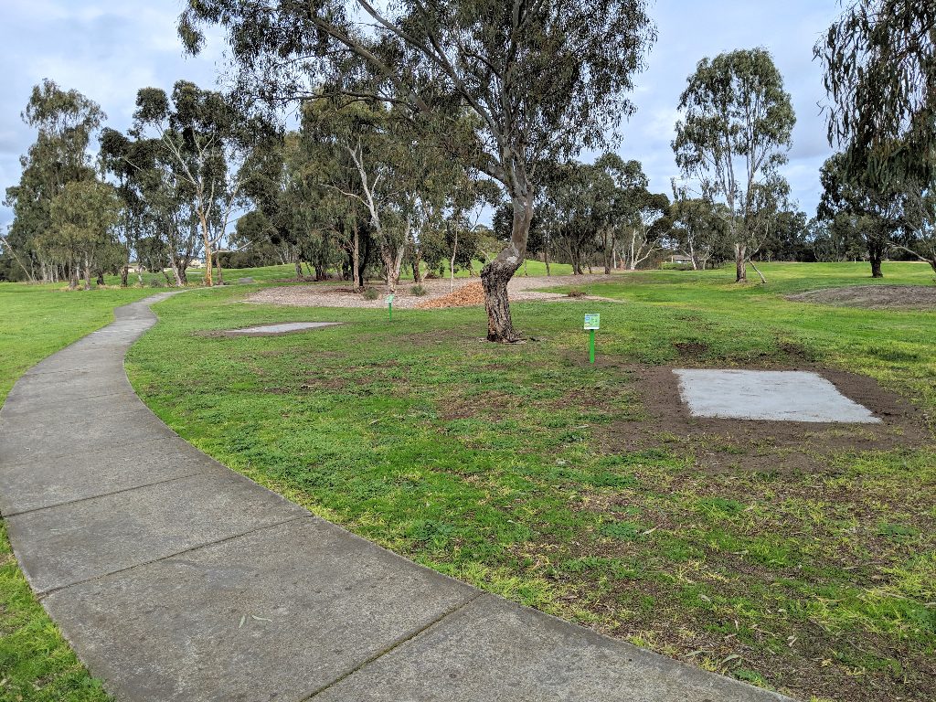 A concrete tee pad set into mown grass beside a path, with gum trees behind.