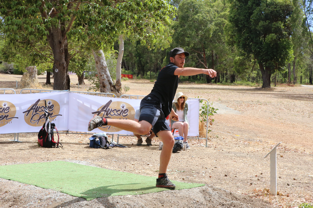 A player throwing from a tee pad at the Aussie Open, event banners lining the fairway behind.