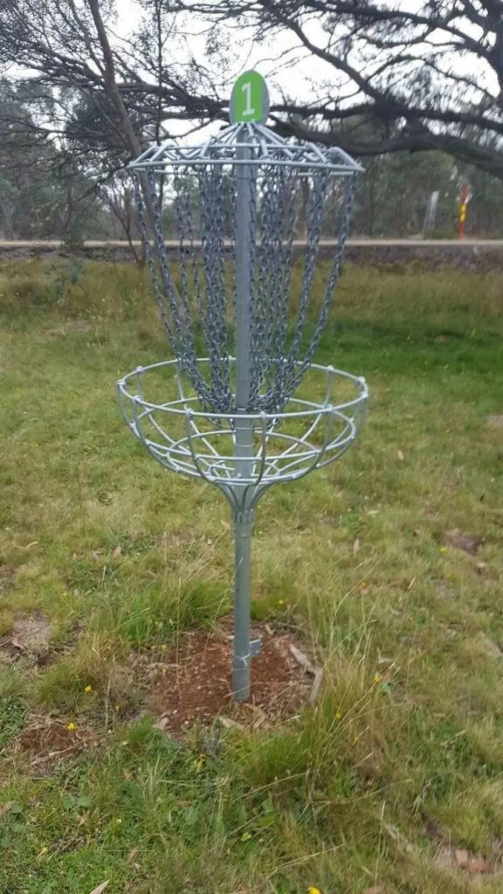 A disc golf basket standing on a grassy alpine slope.