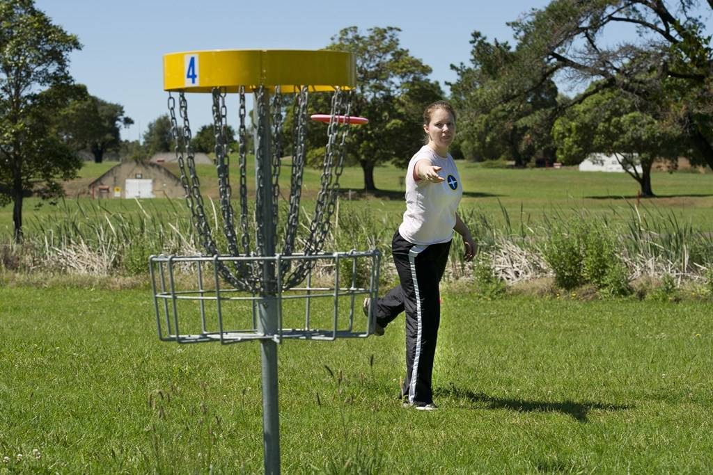 A girl putting into a yellow-topped basket marked hole 4 on open parkland.