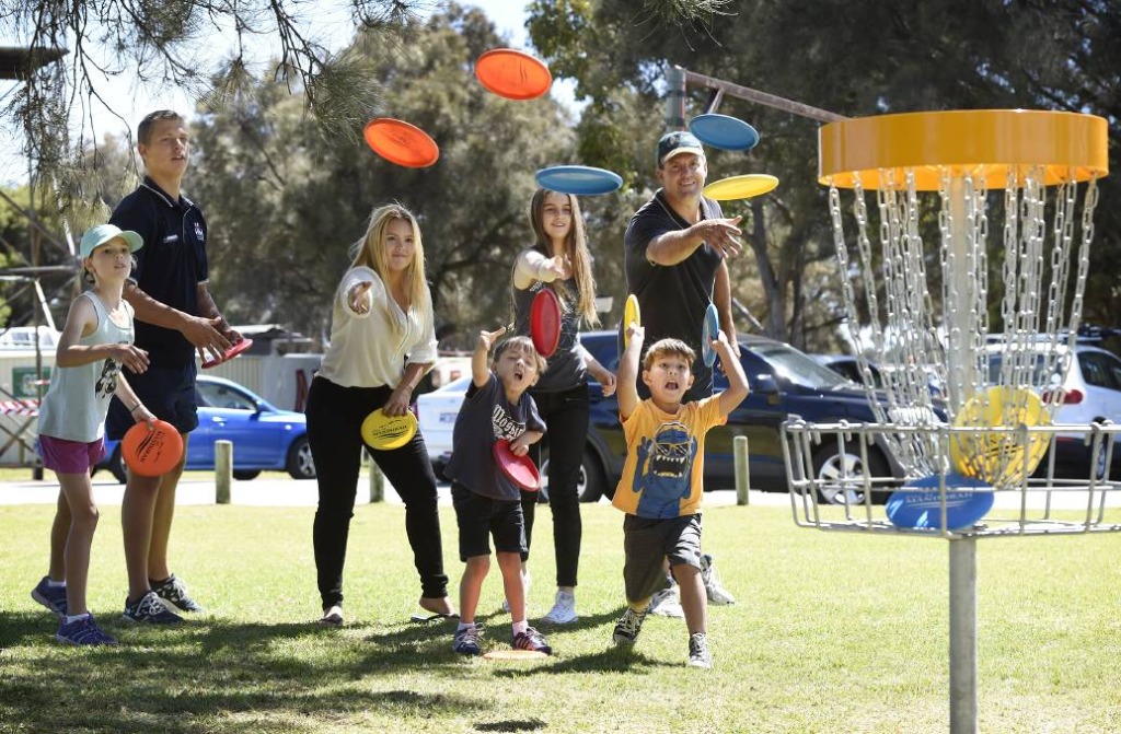 A family throwing discs together towards a basket, several coloured discs in the air at once.
