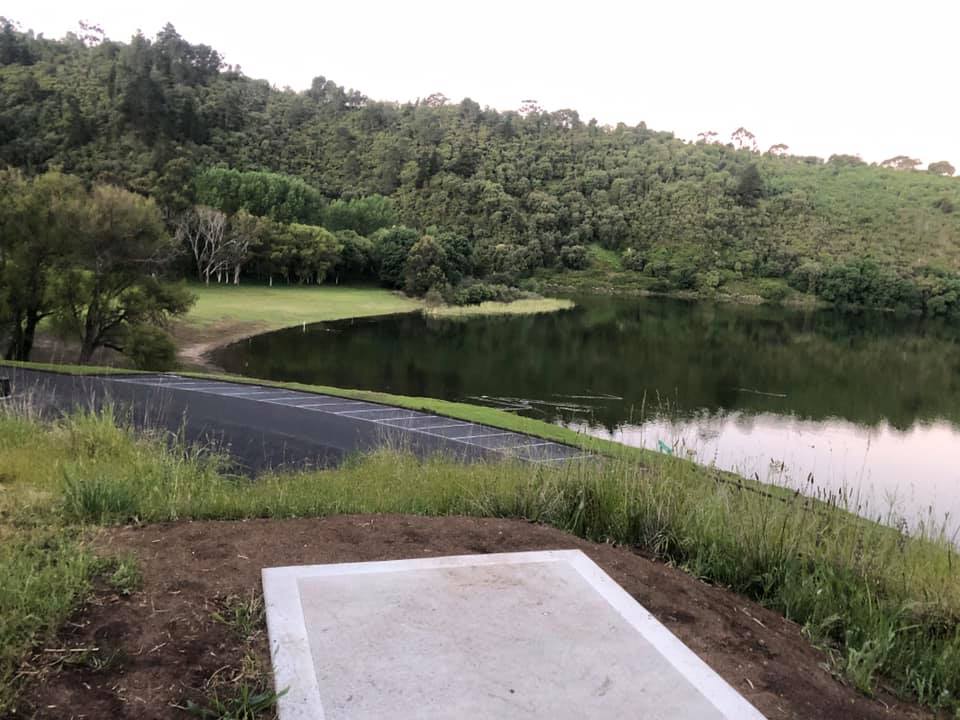 A concrete tee pad beside a lake in a wooded crater.