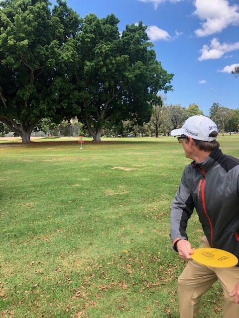 A player winding up to throw a yellow disc across a green fairway.