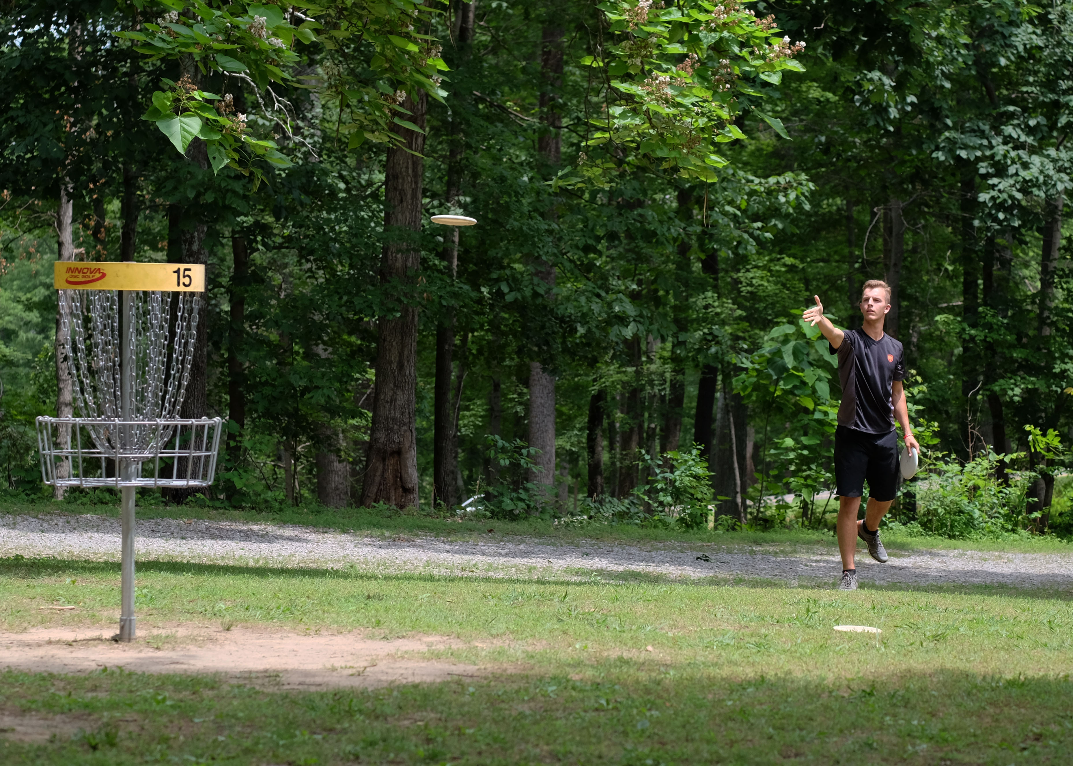 A player celebrating beside a basket marked hole 15 on a woodland path.