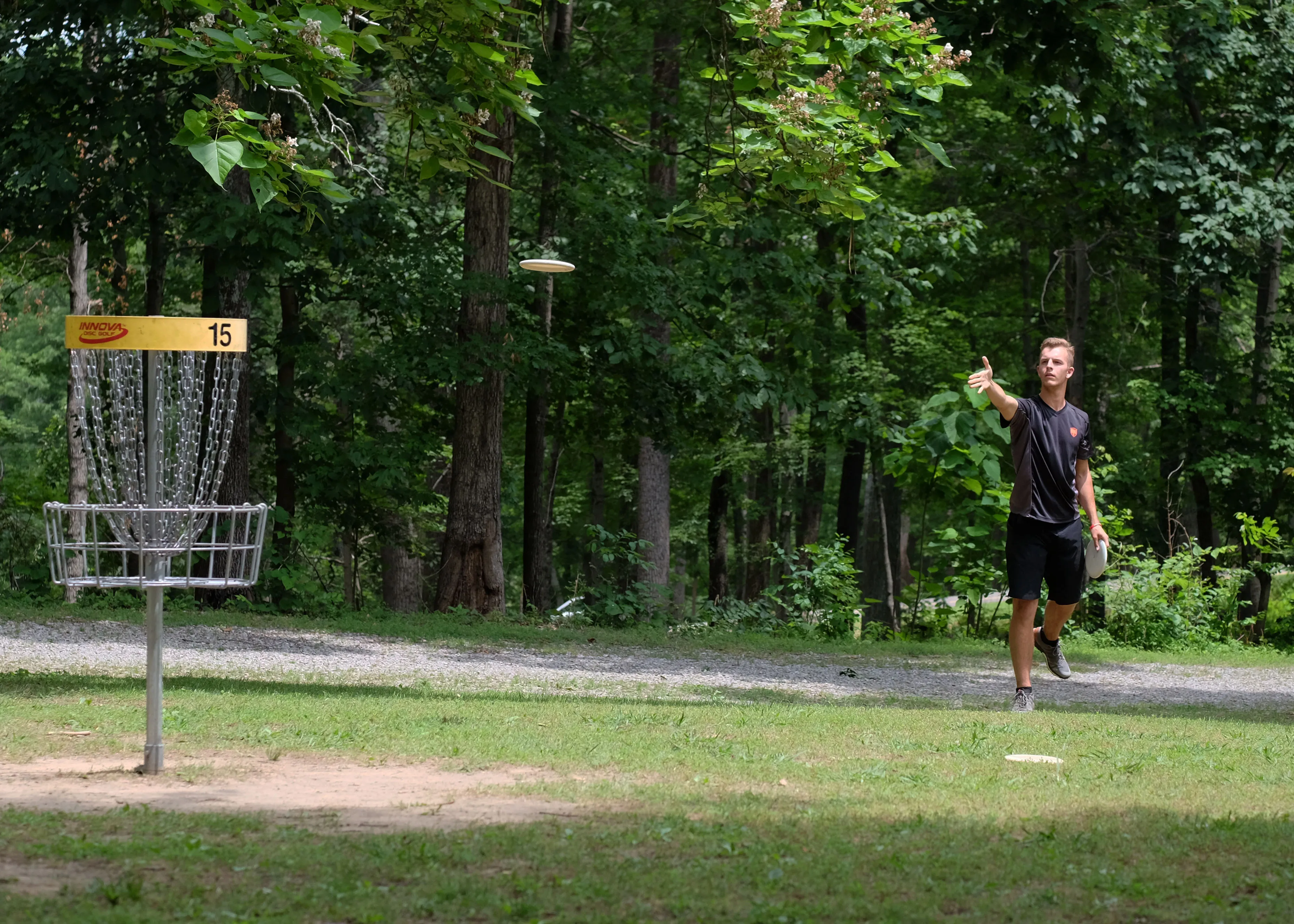 A player celebrating beside a basket marked hole 15 on a woodland path.