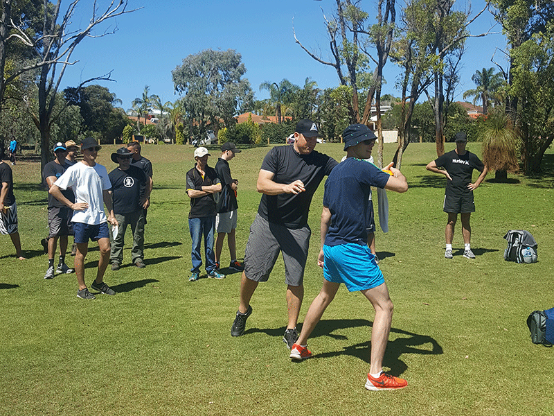 A group of players on a fairway watching one of them demonstrate a throw.