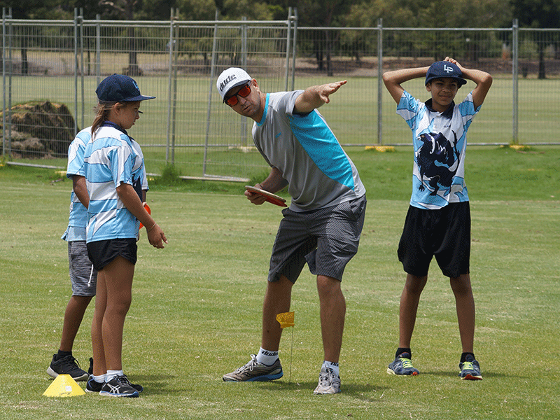 A coach instructing two young players on a field, pointing out the line of the throw.