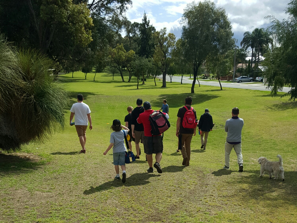 A group of people walking together across a park, a small dog following behind.