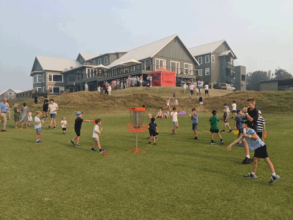 Children playing with discs across a golf course lawn beside the clubhouse.