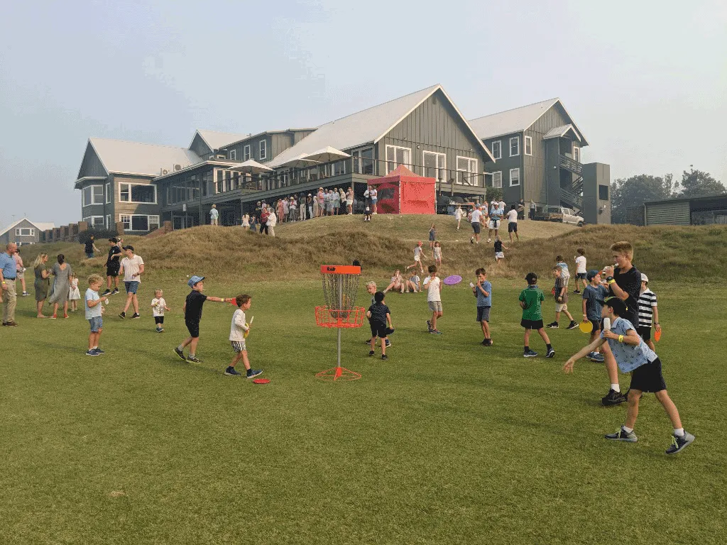 Children playing with discs across a golf course lawn beside the clubhouse.