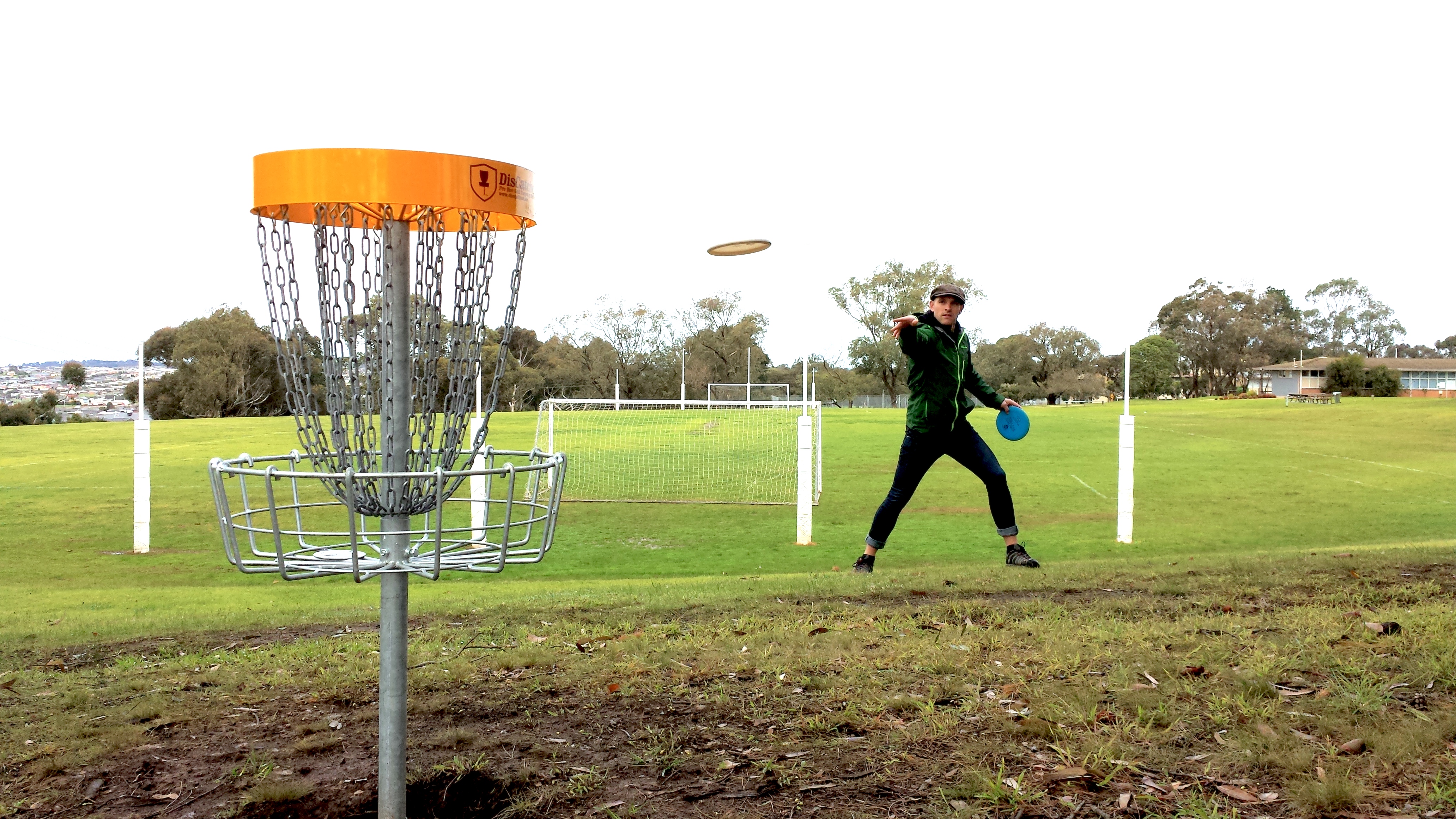 A player throwing on a school oval, the disc in flight towards the basket.