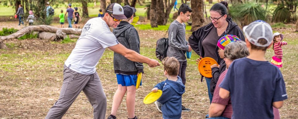 A coach demonstrating a disc golf throw to a group of children and parents at a come-and-try session.