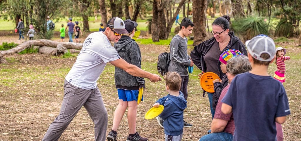 A coach showing a group of families how to throw at an outdoor come-and-try session.