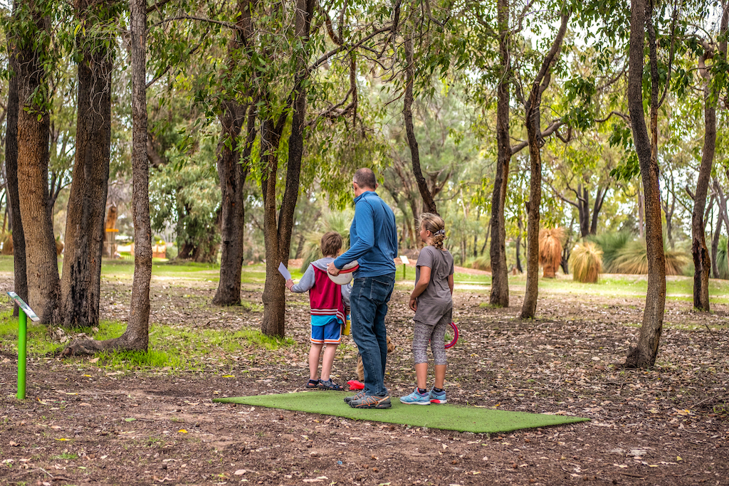 A father and two children standing on a tee pad on a bushland course.