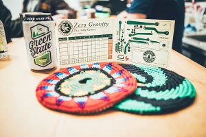 Zero Gravity branded discs, a scorecard and craft beer cans arranged on a bar.