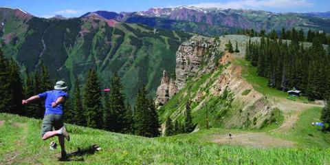 A player throwing a disc from a green mountain slope, ranges rising behind.