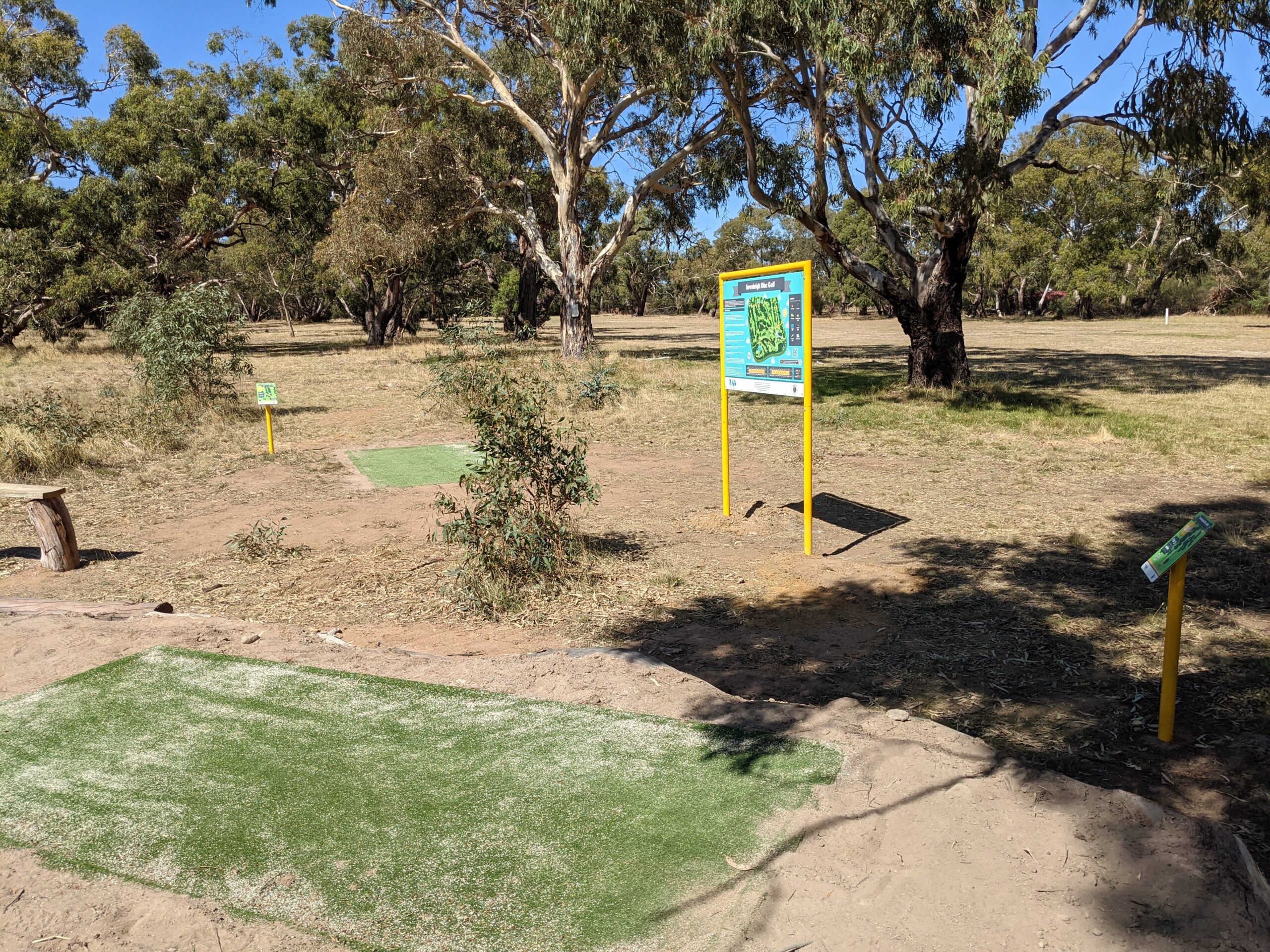 A green tee pad and yellow tee sign set in dry bushland.