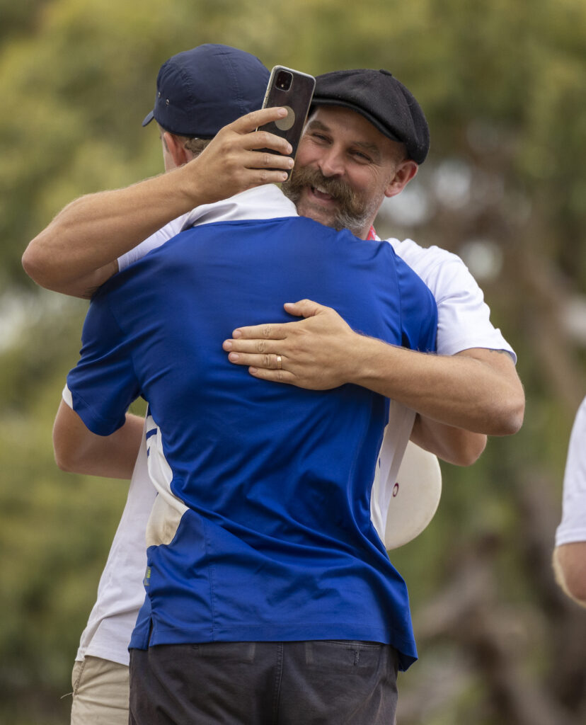 Two players embracing after a round, one holding up a phone to take a photograph.