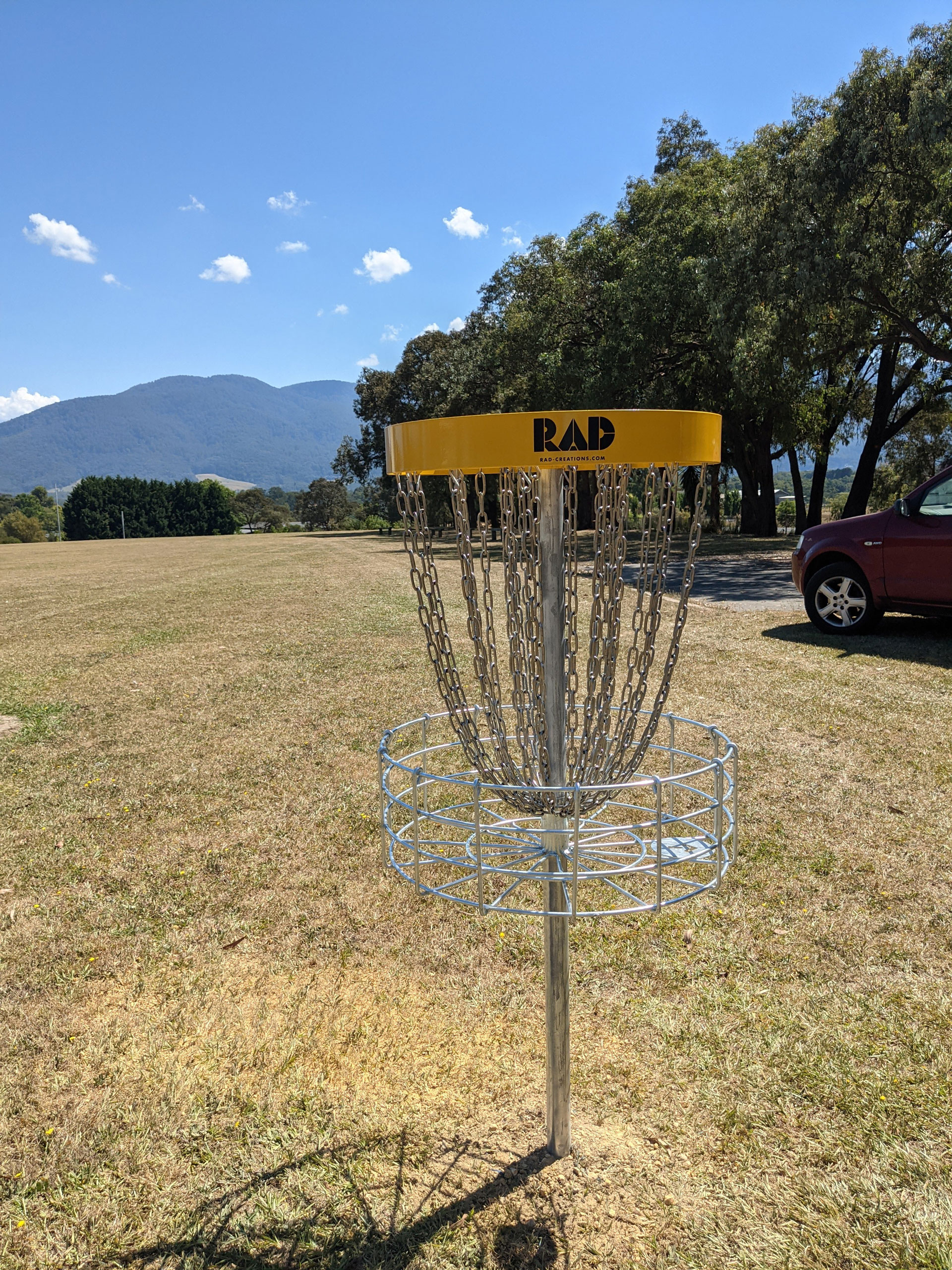 A RAD disc golf basket on a dry school field, mountains in the distance.