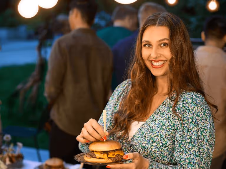 A woman holding a plate with a hamburger on it.