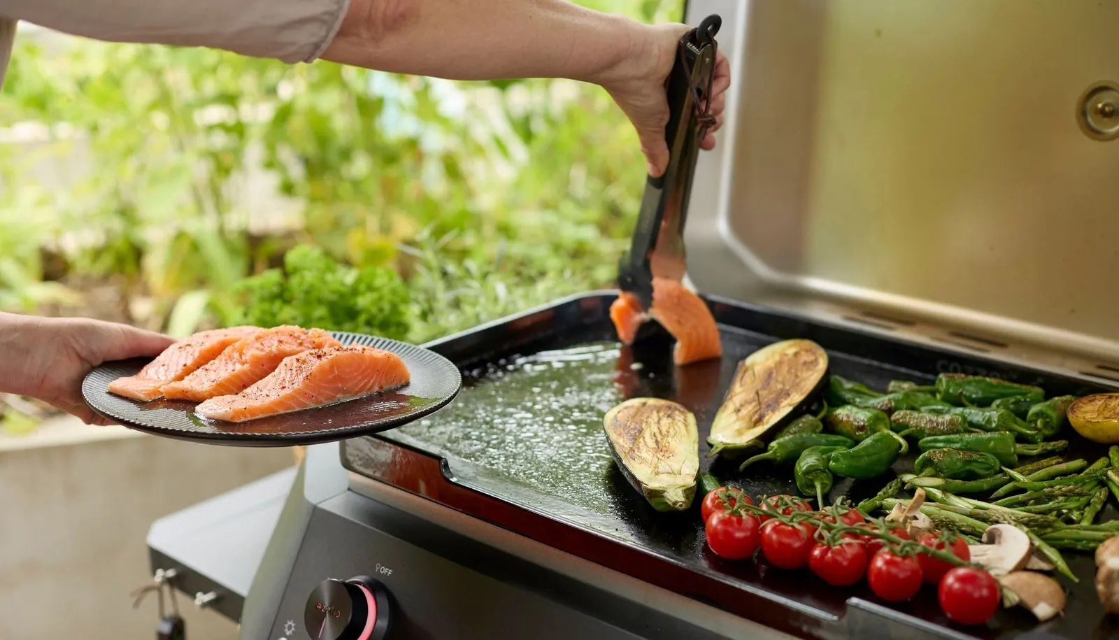 A person holding a plate of food over a grill.