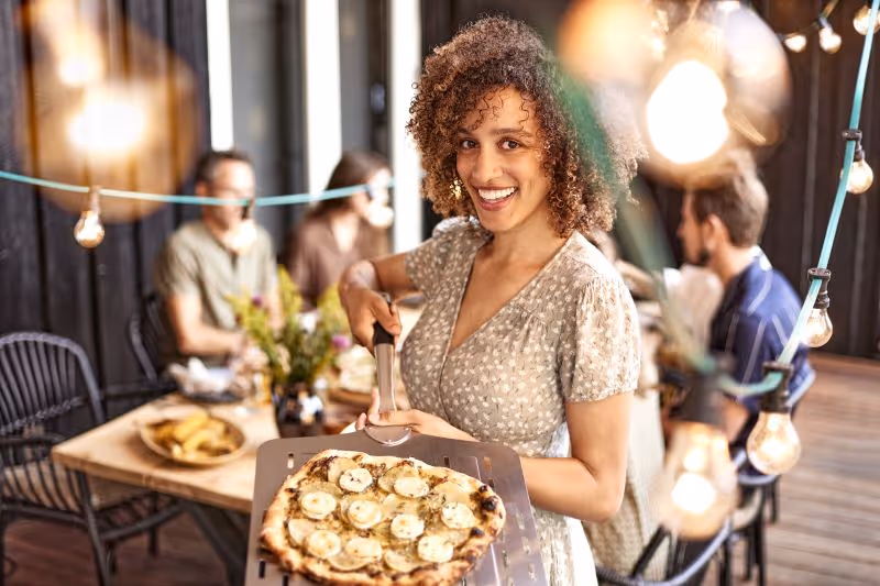 A woman holding a tray with a pizza on it.
