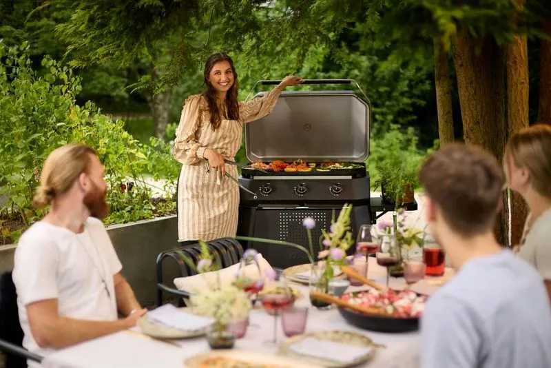 A woman standing in front of an outdoor grill.
