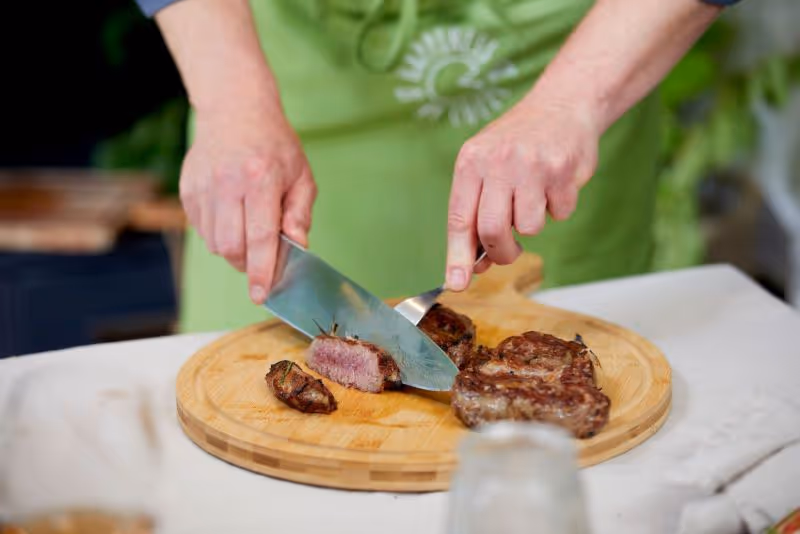 A person cutting meat with a knife on a cutting board.