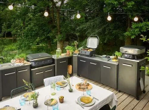 An outdoor kitchen with grills and a table with food on it.
