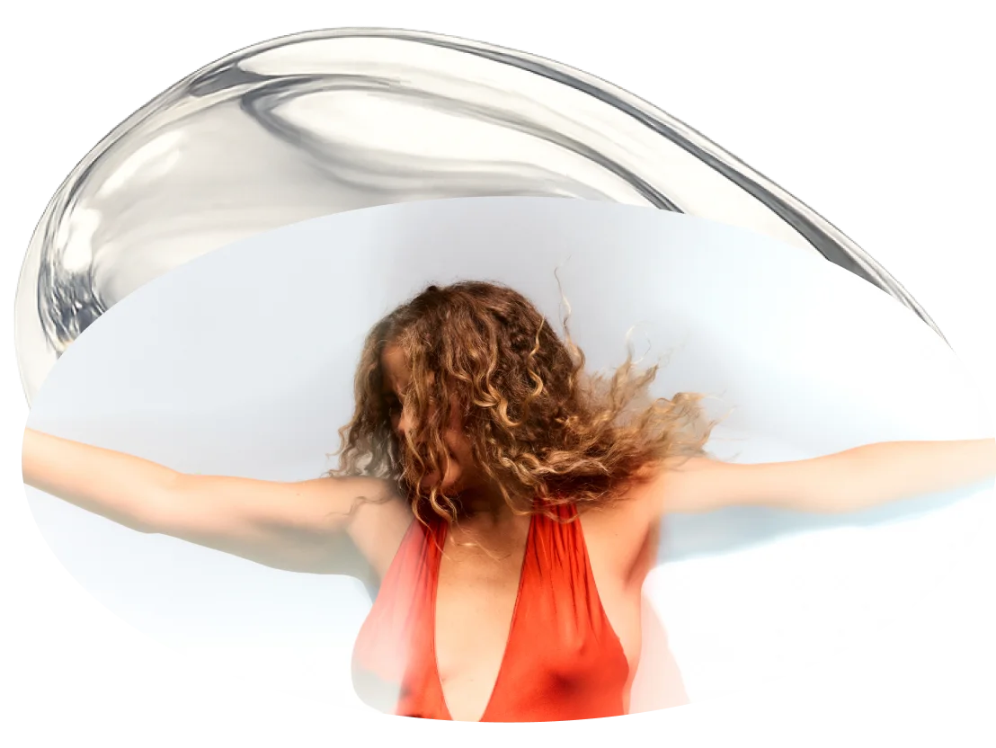 Susana with curly hair wearing a red dress, standing with her arms outstretched against a bright background, framed by an abstract glass shape