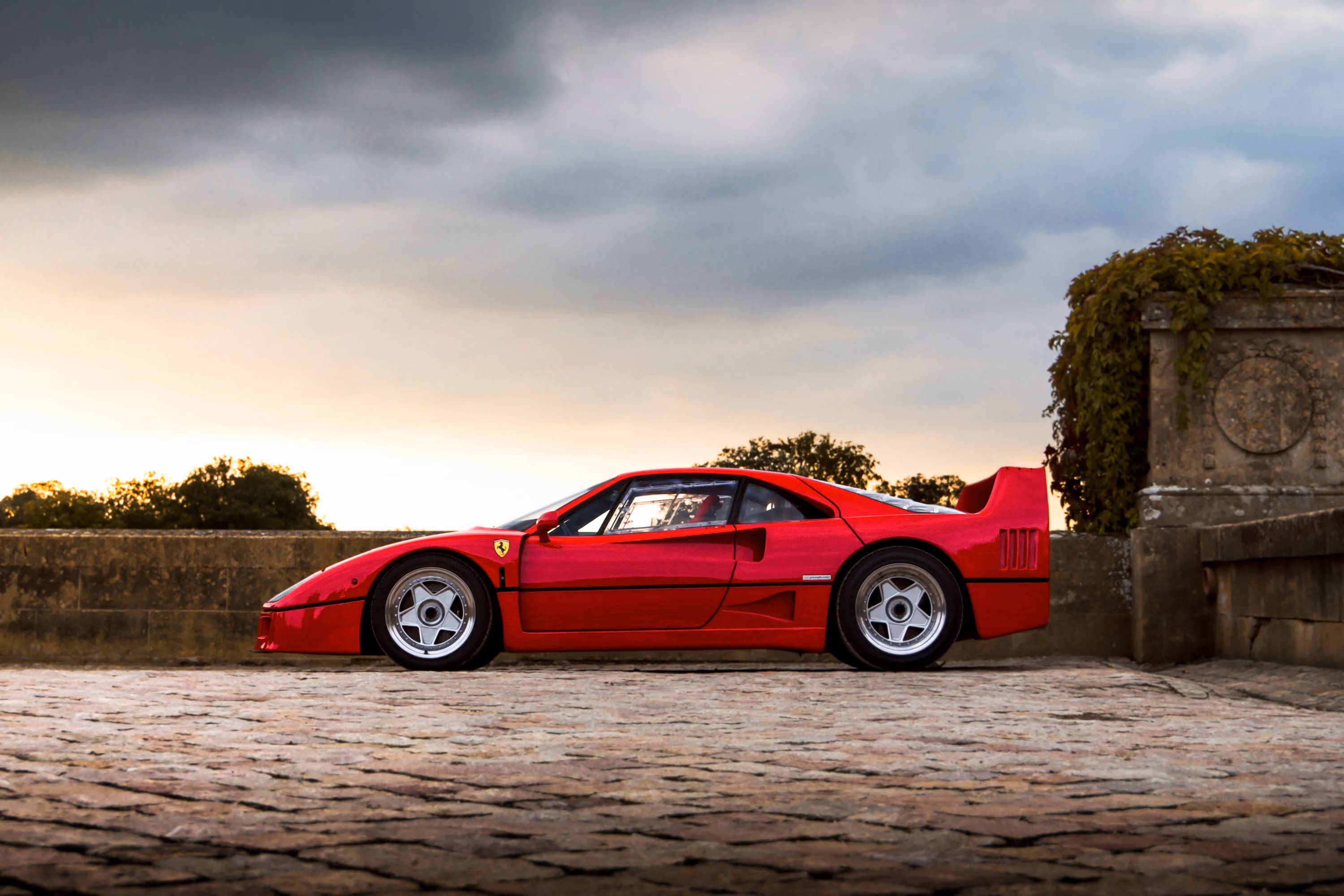 Classic red Ferrari in profile on a cobbled terrace at dusk